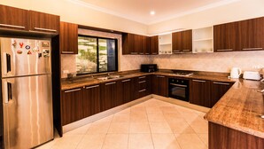 A modern kitchen with dark wooden cabinets, stainless steel appliances, and a granite countertop. - Majestice Pool Villa 4 Bedrooms (Pattaya)