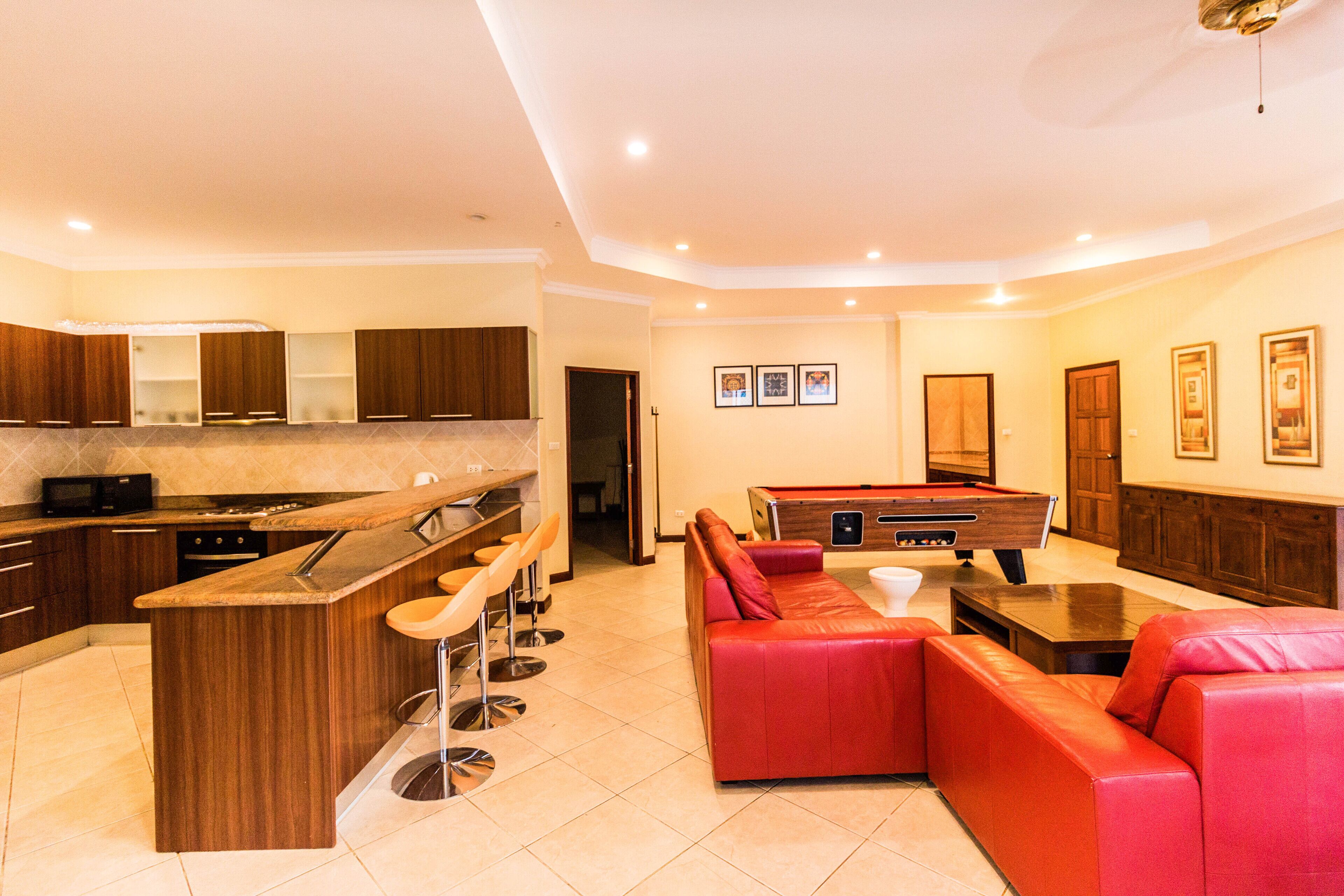 A modern kitchen with a bar area, a pool table, and a red leather sofa.