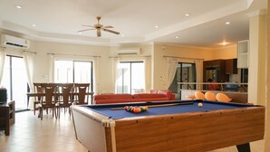 A pool table in a well-lit room with a ceiling fan, a dining area with chairs, and a red sofa. - Majestice Pool Villa 4 Bedrooms (Pattaya)