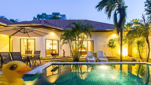 A swimming pool with a duck, chairs, and a table outside a building with a tiled roof and palm trees. - Majestice Pool Villa 4 Bedrooms (Pattaya)