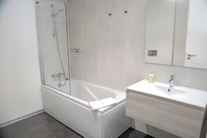 Un baño moderno con ducha envuelta en vidrio, una bañera blanca y un lavabo con espejo.
