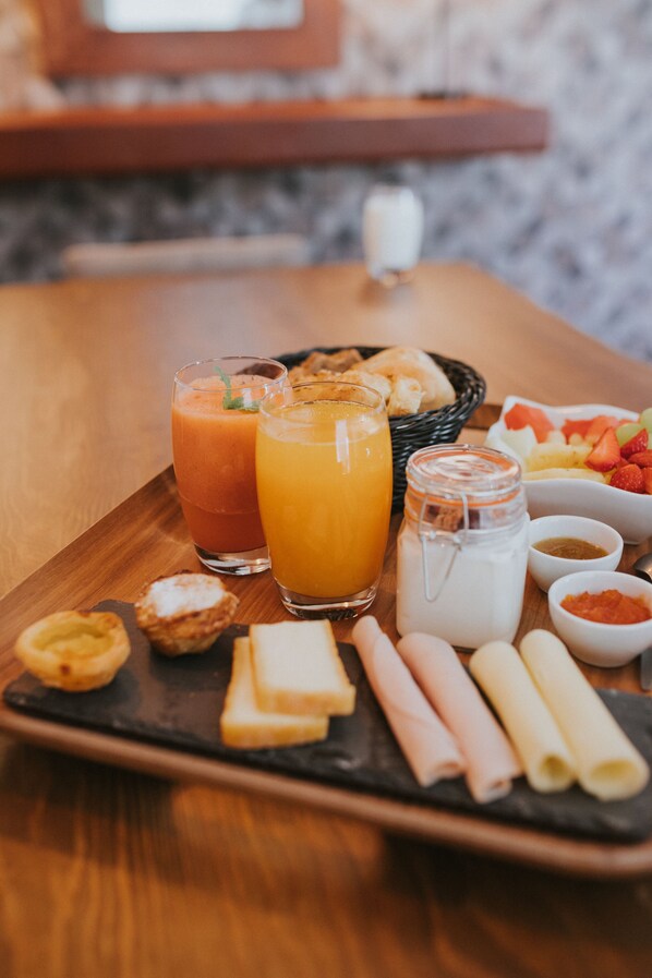A breakfast tray with two glasses of juice, a pitcher of milk, and various pastries and fruits. - O Cantinho dos Cabrais B&B (Belmonte)