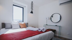 Una habitación de hotel moderna con una cama grande, una manta roja, un espejo redondo y un escritorio con una lámpara.