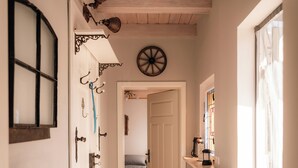 A narrow hallway with wooden beams, a door with hooks, a radiator, and a shelf with a lamp.