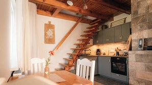 A kitchen with wooden beams, a dining table, chairs, and a stone wall.