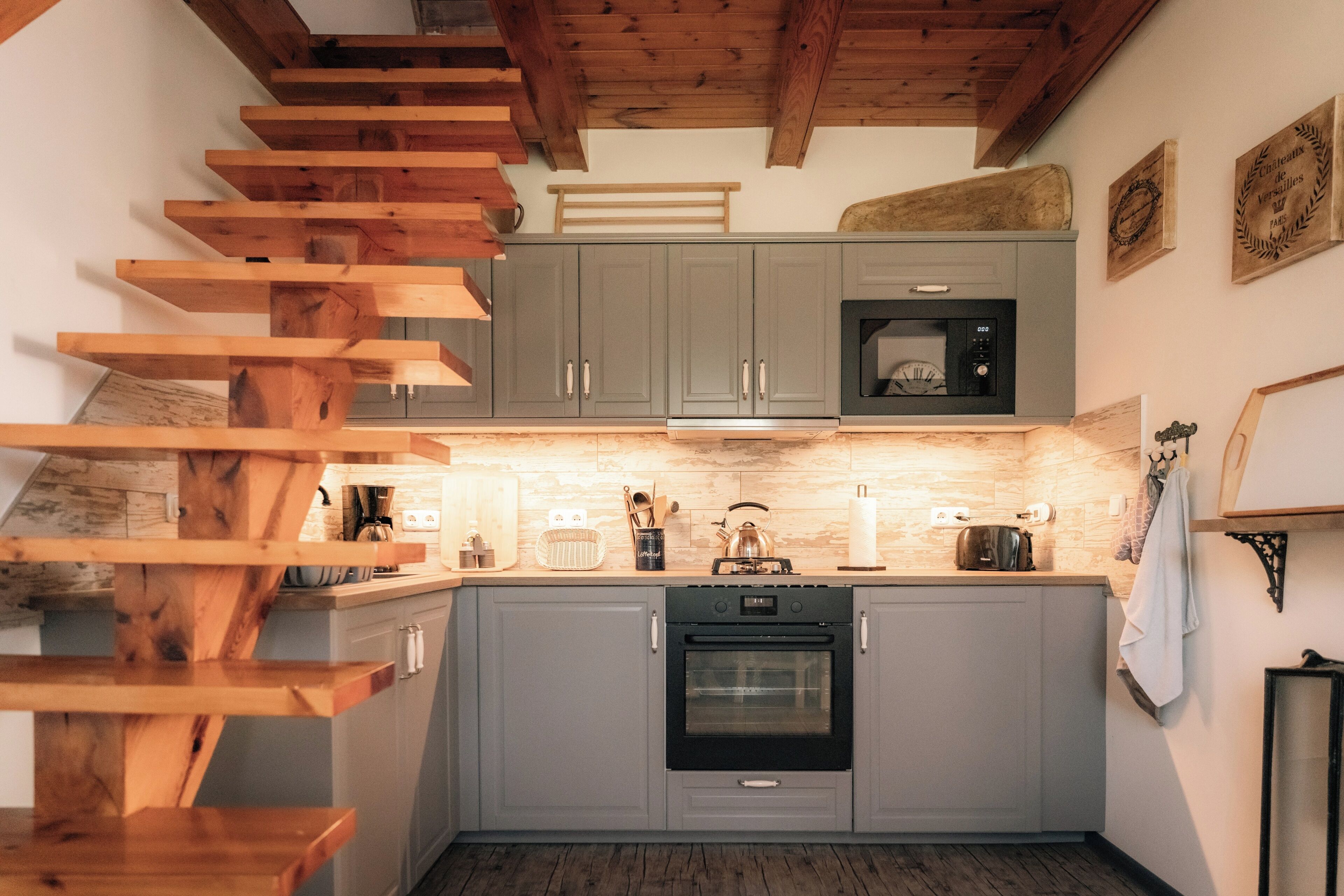 A kitchen with grey cabinets, a black oven, and a wooden staircase.