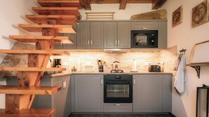 A kitchen with grey cabinets, a black oven, and a wooden staircase.