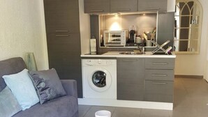 A compact living space with a grey sofa, a glass coffee table, a washing machine, and a kitchenette with a microwave and toaster. - Studio Center Cannes Terasse (Cannes)