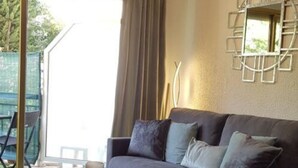 A modern living room with a grey sofa, a small round table, and a glass coffee table. There is a sliding glass door leading to an outdoor area. - Studio Center Cannes Terasse (Cannes)