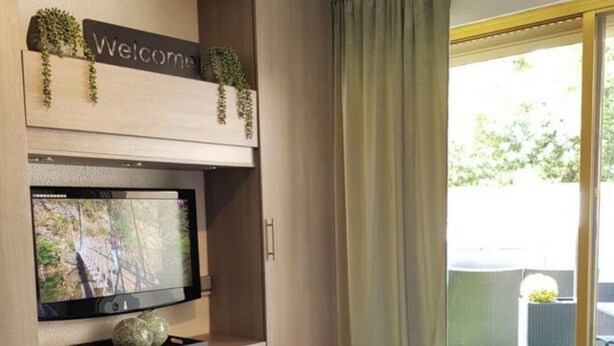A modern room with a TV mounted on a wooden wall, a small table, and a sliding glass door leading to an outdoor area. - Studio Center Cannes Terasse (Cannes)