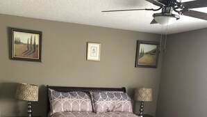 A bedroom with a wooden bed, two bedside tables with lamps, a ceiling fan, and two framed pictures on the walls. - 228 BEAUTIFUL DOWNTOWN AIR/WIFI/close to FALLS (Buffalo)
