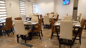 A dining area with multiple tables and chairs, air conditioning units on the walls, and a television mounted on the wall.