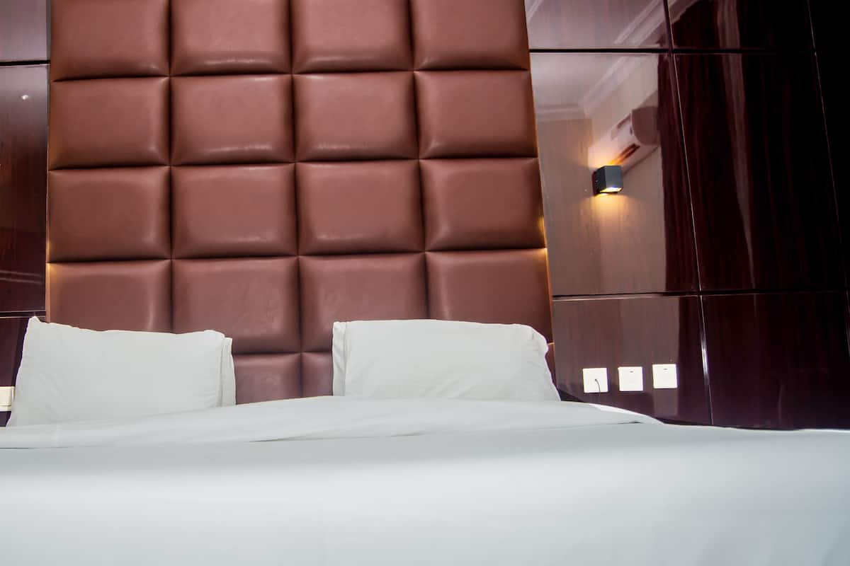 A hotel room with a large bed, a padded headboard, and a wall-mounted light fixture.