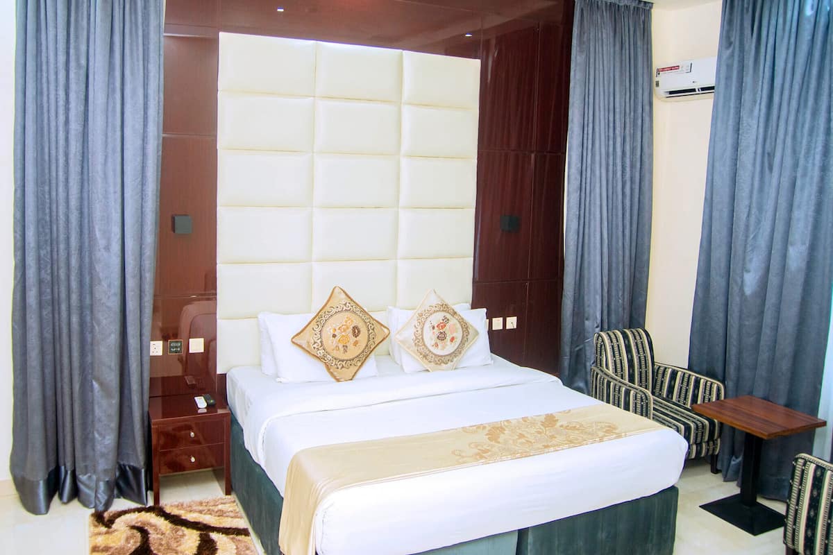 A hotel room with a large bed, two decorative pillows, a small table, and a chair.