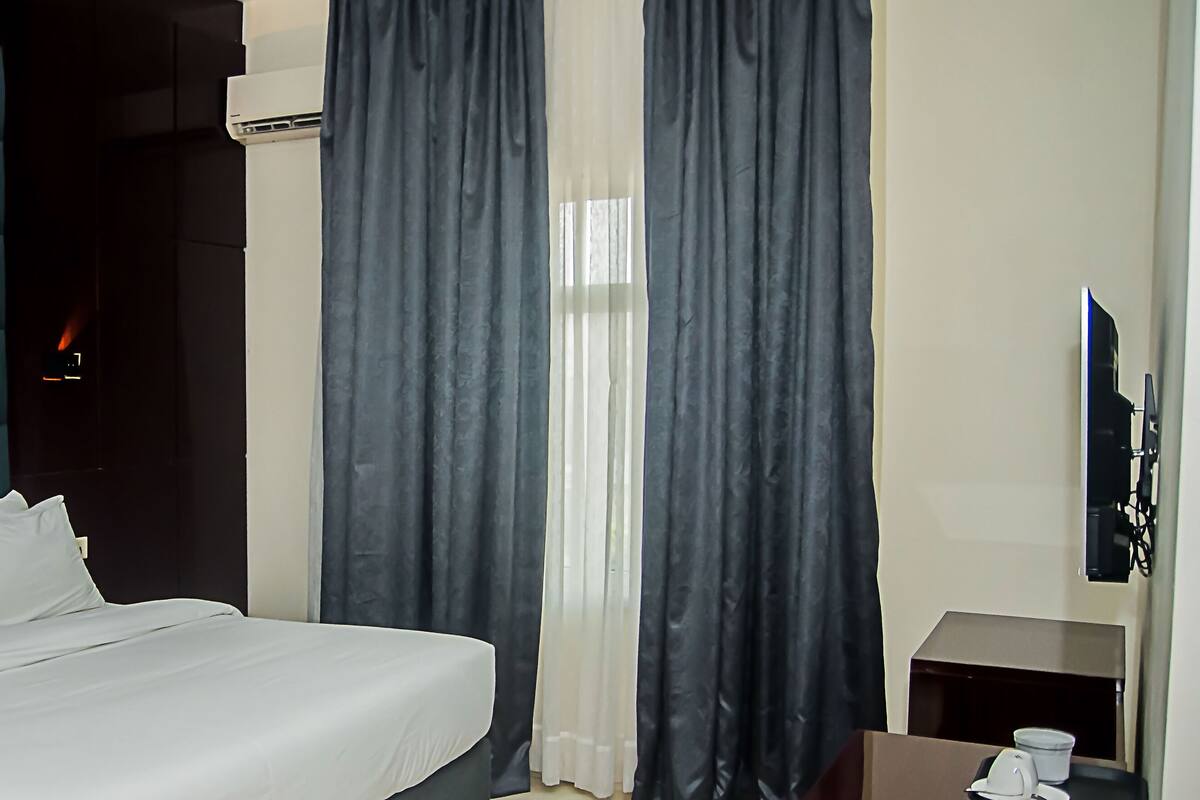 A hotel room with a bed, a nightstand, a TV, and a window with curtains.