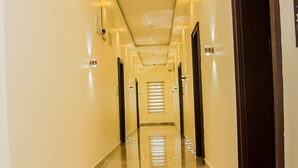 A long, well-lit hallway with a polished marble floor, leading to a set of doors.