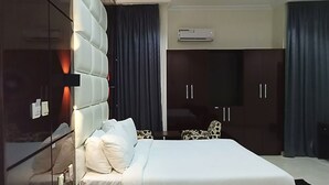 A modern hotel room with a large bed, dark wooden wardrobe, and an air conditioning unit.