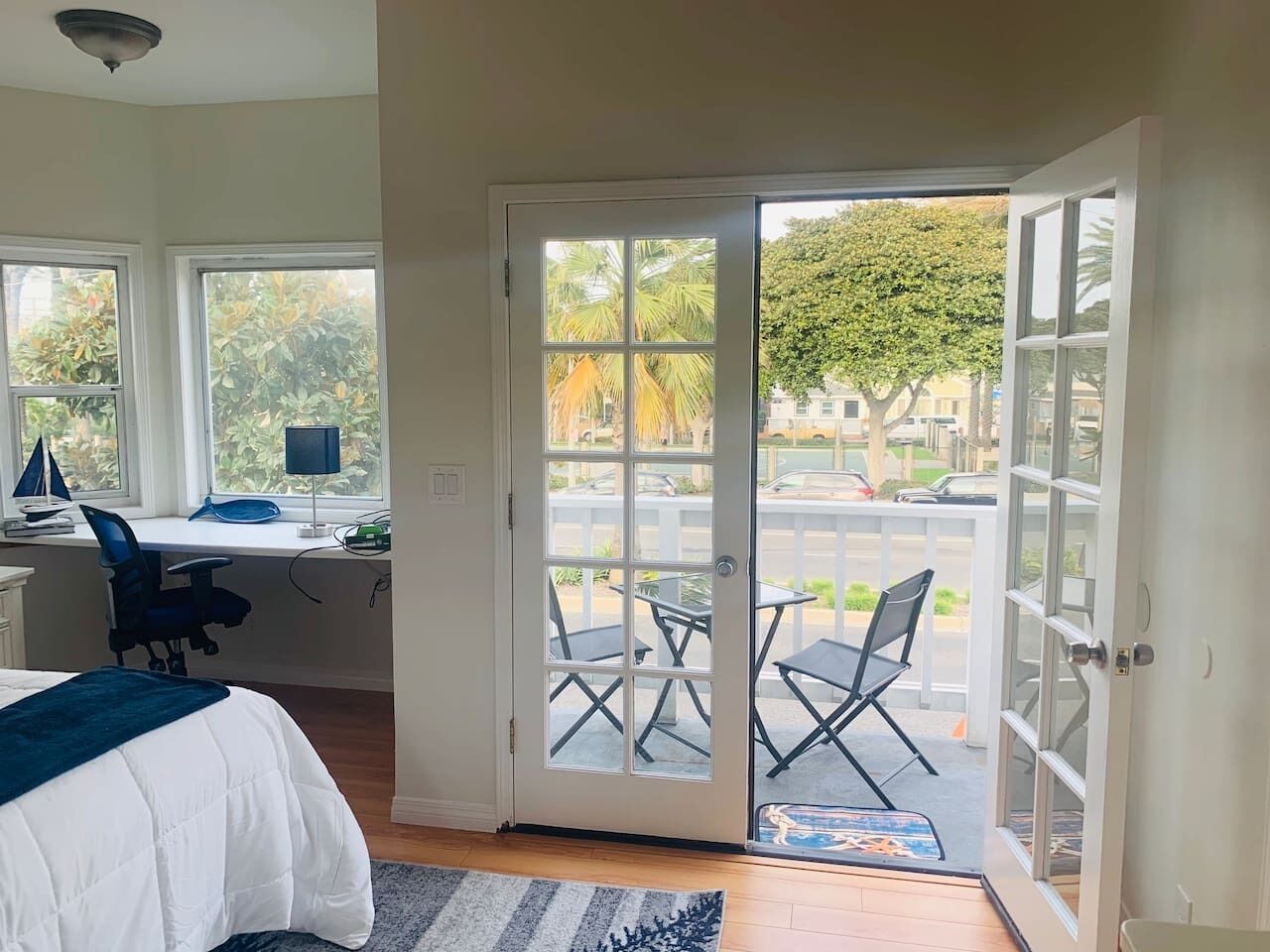 A bedroom with a bed, desk, and chair, a balcony with chairs, and a door leading outside.