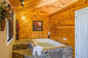 Un baño con lavamanos de piedra, una bañera, paredes de madera, una ventana con persianas y una puerta.