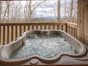 Un jacuzzi en una terraza de madera con vistas a árboles y montañas al fondo.