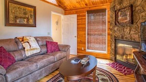A cozy living room with a stone fireplace, wooden ceiling, and a comfortable sofa. - GreatView!PoolTable,HotTub,Privacy,Fireplace (Sevierville)