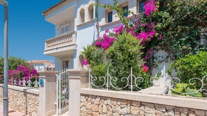 Un edificio a due piani con muro in pietra e cancello in metallo, con fiori rosa e vegetazione.