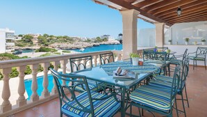 Una terrazza con tavolo e sedie in vetro, affacciata su una vista costiera con edifici e un litorale roccioso.
