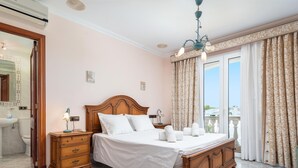 Una camera da letto con un letto di legno, un comodino, una cassettiera, un bagno con lavandino e WC, e un balcone con tende.