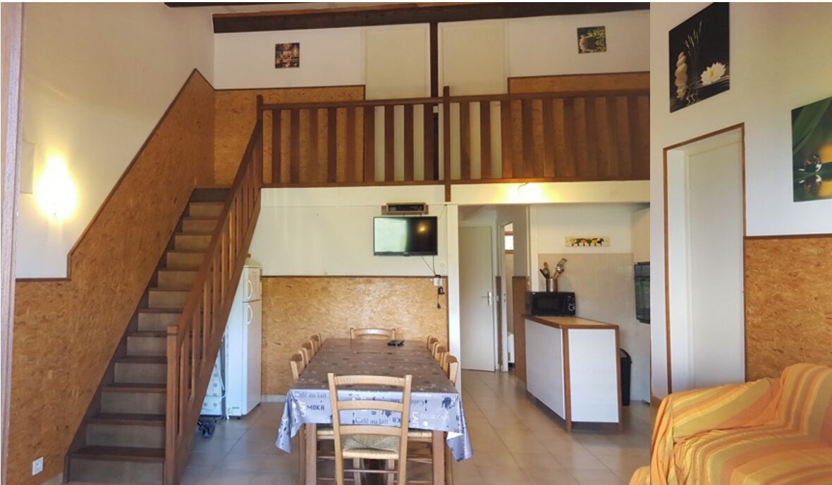 Ein Essbereich mit einer Holztreppe, einem an der Wand befestigten Fernseher und einer Küchenzeile mit Kühlschrank und Mikrowelle.