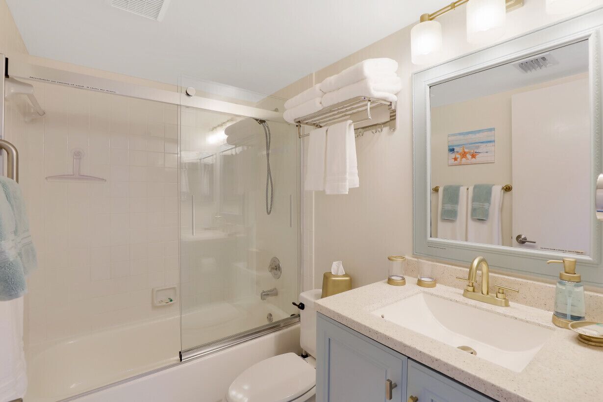 A modern bathroom with a glass-enclosed shower, a white sink with gold fixtures, and a large mirror.