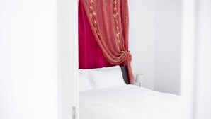 A bed with white linens, a red canopy, and a bedside table with a lamp.