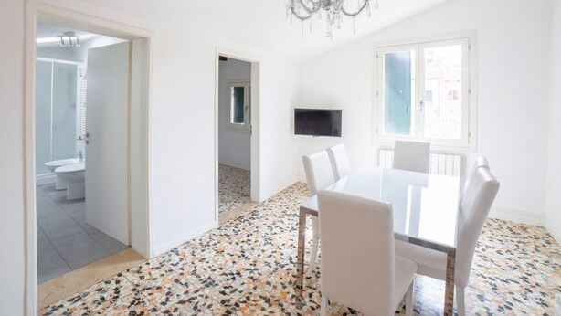 A room with a dining table, chairs, a TV, a chandelier, and a bathroom visible through an open door.
