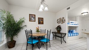 A dining area with a round table, four chairs, a potted plant, and two wall-mounted light fixtures. - Sun Ray #1B - Pet Friendly, 3min Walk to Beach (South Padre Island)