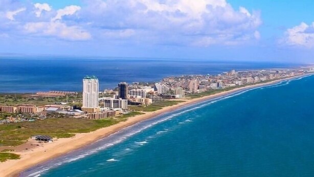 A coastal cityscape with a beachfront hotel, a prominent tall building, and a long stretch of beach. - Sun Ray #1B - Pet Friendly, 3min Walk to Beach (South Padre Island)