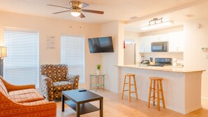 A compact living space with a sofa, armchair, dining table, kitchen area with a microwave, and a ceiling fan. - Sun Ray #3A - Pet Friendly, 3min Walk to Beach (South Padre Island)