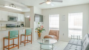 A modern kitchen with a microwave, stove, and bar area. There is a dining table with chairs and a sofa in the living area. - Sun Ray #3B - Pet Friendly, 3min Walk to Beach (South Padre Island)