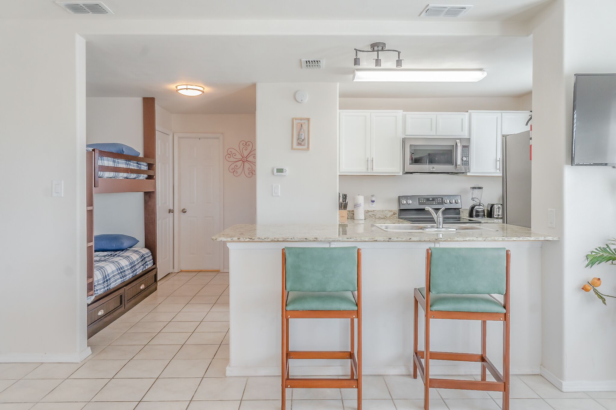 A compact kitchen with white cabinets, a microwave, and a refrigerator. There is a small bar area with two stools.