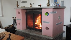 A fireplace with a pink facade, a visible fire, and decorative items on top. - Holiday house with big garden, Resa Valley, Locarno (Brione sopra Minusio)