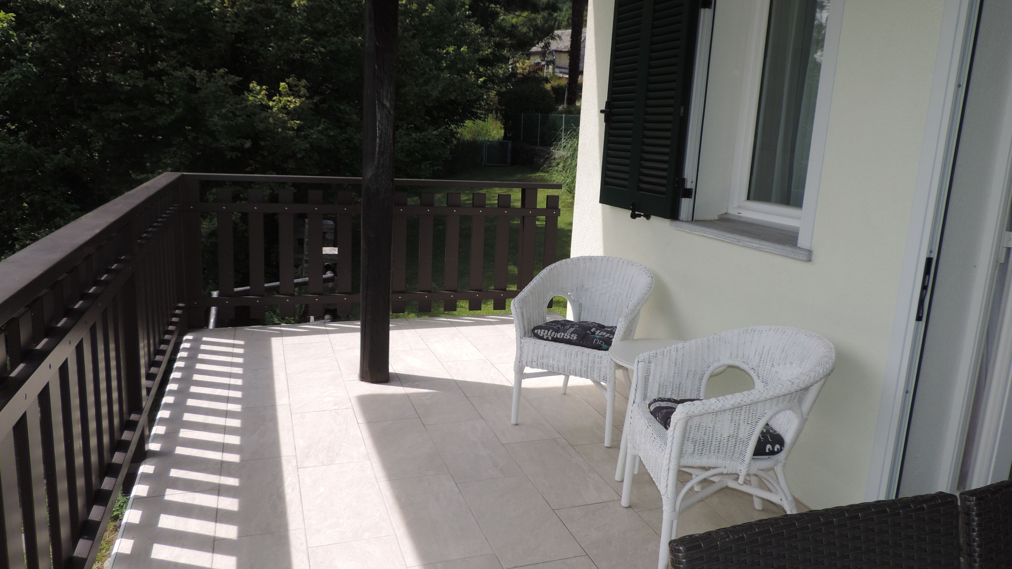A balcony with two wicker chairs, a wooden railing, and a window with shutters.