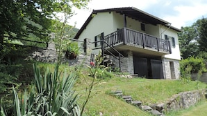 A two-story house with a balcony, stone walls, and a garden with various plants. - Holiday house with big garden, Resa Valley, Locarno (Brione sopra Minusio)