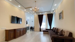 Amplia sala de estar con cocina moderna, un televisor de pantalla plana grande, un conjunto de sofás y una araña.