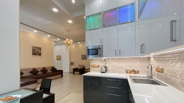 Una cocina moderna con una isla central, un comedor con mesa y sillas, y una sala de estar con sofá y candelabro.