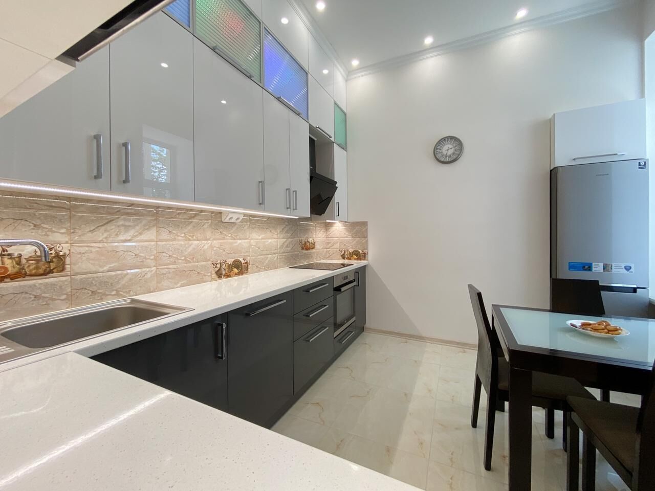 Een moderne keuken met een inbouwoven, een spoelbak en een eethoek met een tafel en stoelen.