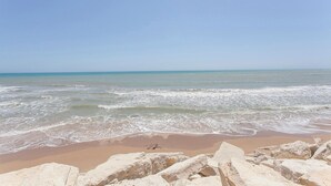 Una spiaggia con onde, cielo sereno e formazioni rocciose in primo piano.