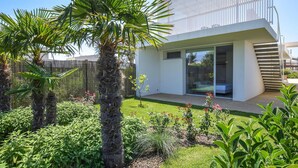 Una casa moderna con un'ampia porta in vetro, un piccolo patio e un giardino curato con diverse piante e una palma.