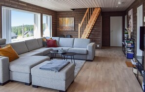 Relax in a stylish living space with a sofa, ottoman, and TV, surrounded by a serene forest view.