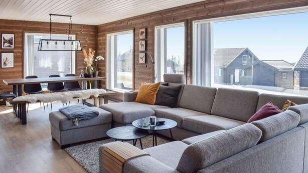 A modern living room with a sectional sofa, a round coffee table, and a dining area with a wooden table and chairs. - 4 bedroom cozy home in Sjusjøen (Sjusjøen)