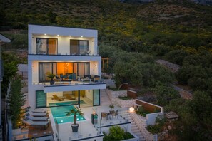 Une maison moderne à deux étages, dotée d’une piscine, d’un espace extérieur aménagé et offrant une vue sur le paysage environnant.
