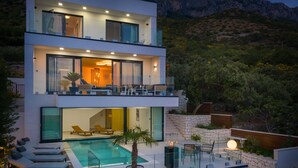 A modern two-story house with a swimming pool, outdoor seating, and a view of the surrounding hills. - LUXURY VILLA BLUE MOON (PODACA)