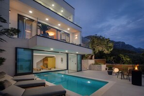 Une maison moderne à deux étages dotée d’une piscine, d’un espace extérieur aménagé et offrant une vue sur les montagnes.